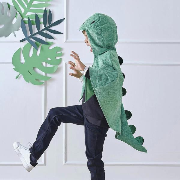 ide view of a child in mid-stride wearing a plush green dinosaur costume cape with scales, spines, and a character hood.