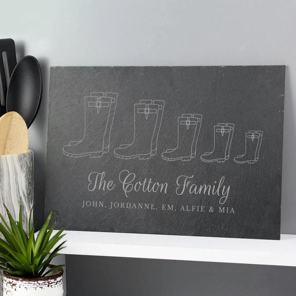 A dark grey hand-cut natural slate board engraved with five pairs of Wellington boots in descending sizes, reading The Cotton Family and individual names below.