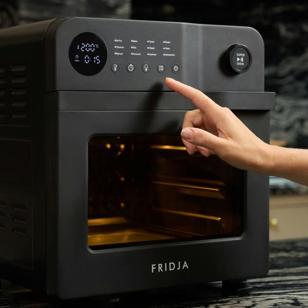 A hand presses a button on the control panel of the black Fridja f66 Super Oven 15L Digital Air Fryer Oven with digital display, PFAS free and ideal for convection cooking, in a modern kitchen.