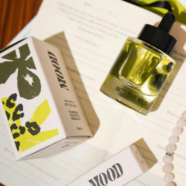 Flatlay shot of Into the Wild Daily Aromatherapy Mood Oil bottle and box alongside a journal, rose quartz beads, and a book by Abode Home & Gifts