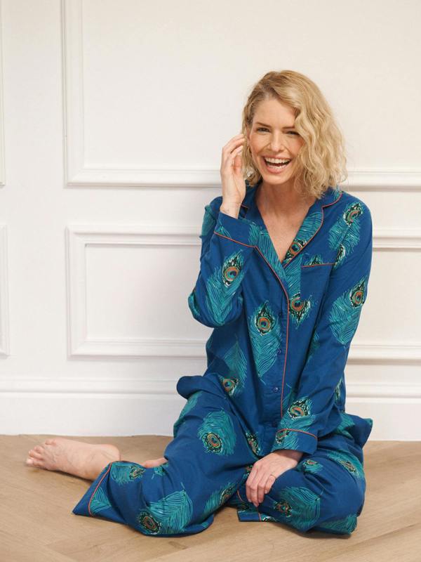 Woman wearing blue pyjamas with peacock patterns sitting on a wooden floor.