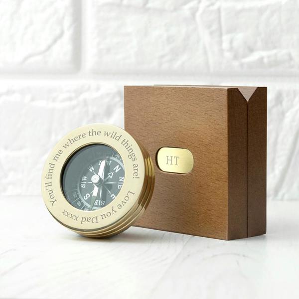 Personalised brass compass engraved with 'You'll find me where the wild things are' resting next to a wooden box with an engraved HT monogram plate