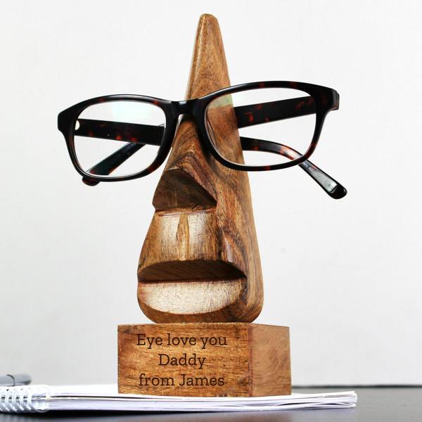 Personalised nose-shaped acacia wood glasses holder resting on a desk with tortoiseshell spectacles resting on the bridge.