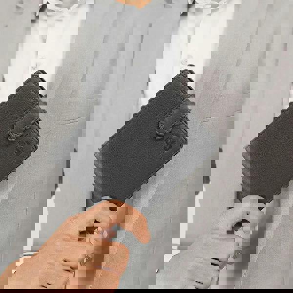 Person holding a black leather wallet with a visible brand logo.