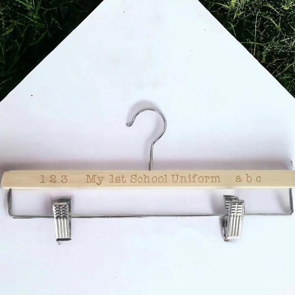 Laser-engraved wooden uniform clip hanger reading "1 2 3 My 1st School Uniform a b c" on a white background with grass border.