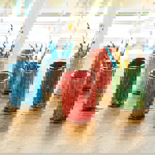Four colorful recycled plastic tumblers with paint brushes and pencils on a wooden table.
