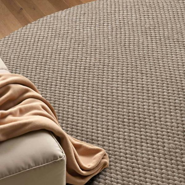 Beige textured rug with a beige blanket draped over a corner of a sofa.