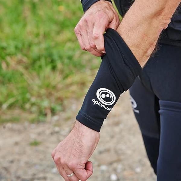 Person outdoors pulling on a black Optimum Hawkley arm warmer with white logo, lifestyle shot - Optimum