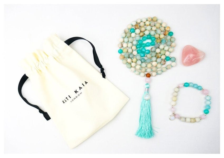 Kati Kaia Crystal Mala Necklace with pastel beads and turquoise tassel next to bracelet and pouch