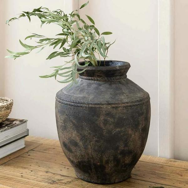 Large rustic antique brown vase with textured stitching details styling green Eucalyptus stems on a wooden table