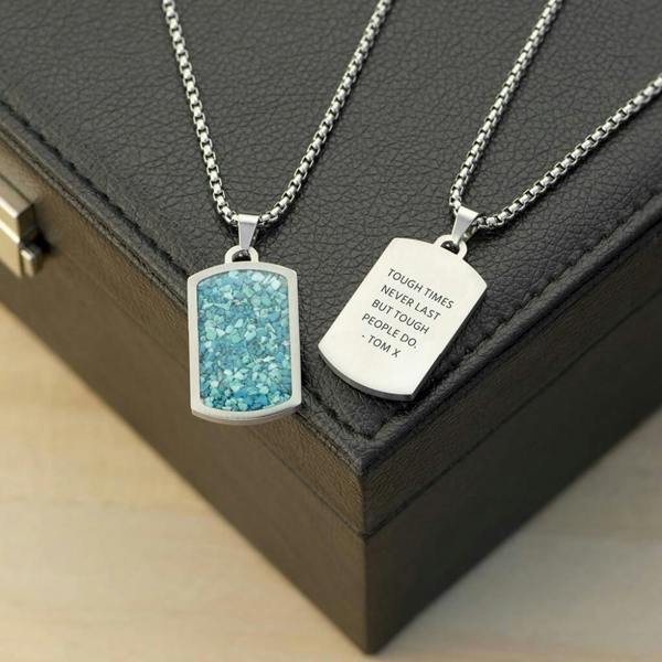 Two silver stainless steel dog tag necklaces displayed on a black leather gift box, one showcasing a vibrant inlaid crushed blue turquoise stone and the other showing a personalised engraved message on the smooth reverse side.