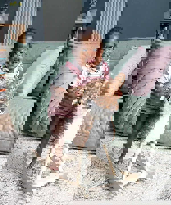 Toddler riding on baby rocking animal toy in front of green sofa