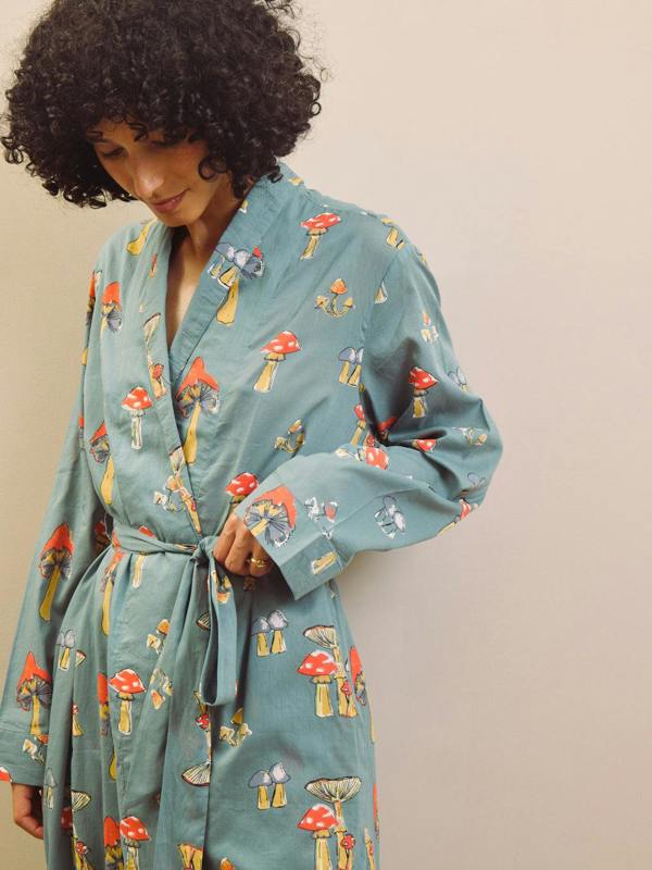 Woman wearing a grey robe with mushroom pattern against a plain background