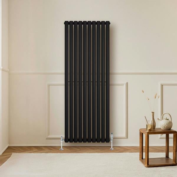 Sleek black oval single column radiator with vertical bars, complemented by chrome valves, set against a neutral wall and wooden floor