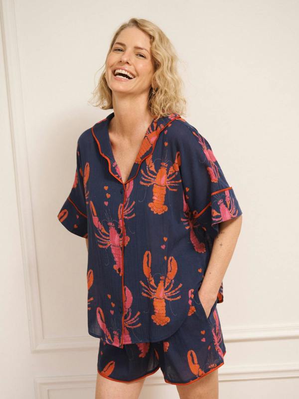 Model wearing navy gauze shortie pyjamas with a playful lobster and heart print, featuring a relaxed short-sleeve button-up shirt and matching shorts.