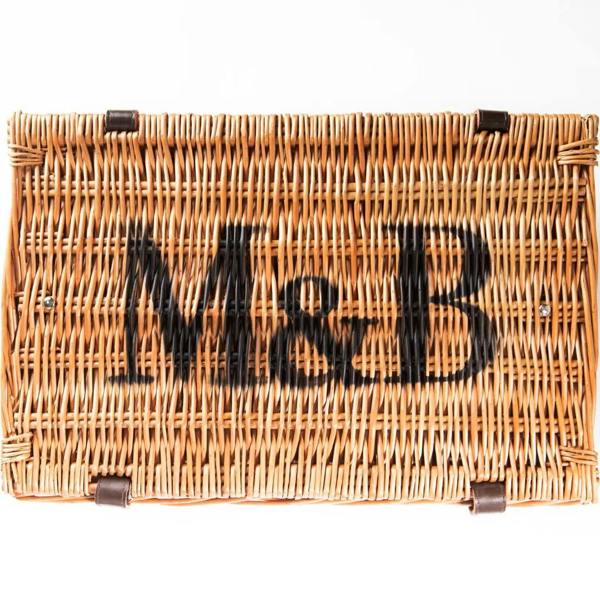 Closed traditional wicker hamper basket with leather straps stencilled with the Marshall and Brown M&B logo on top.
