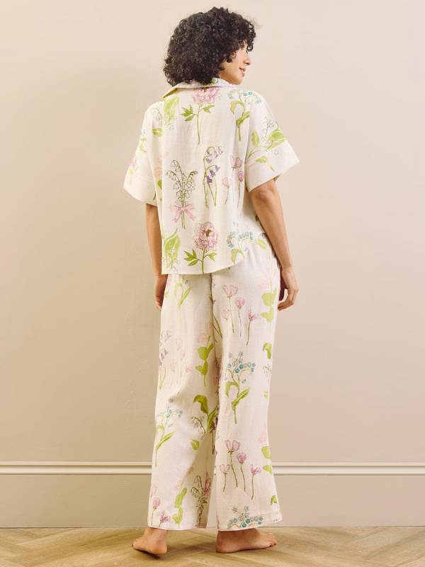 model wears relaxed fit pyjama set in a pretty floral print against a beige wall. Back detail