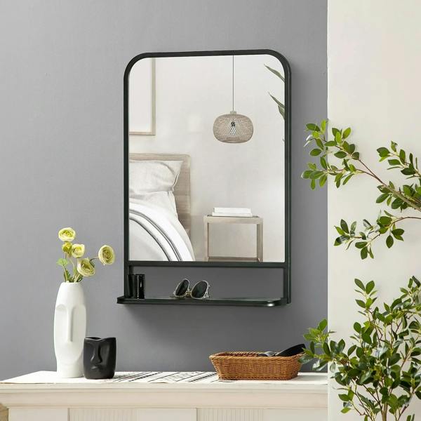 Black wall mirror with storage shelf, reflecting indoor items and plants.