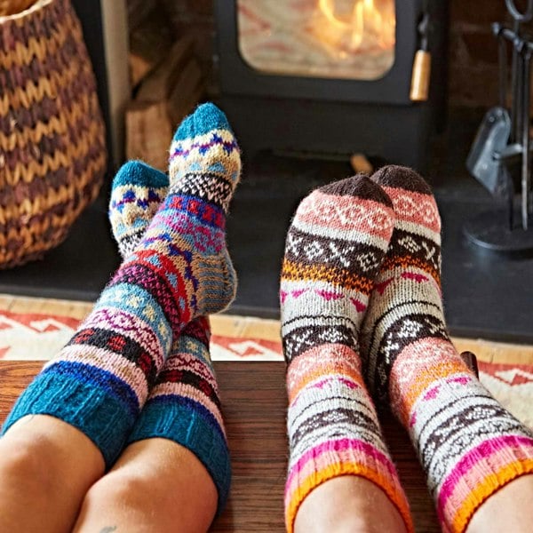 Two people wearing hand knitted Woollen Fairisle Socks by Paper High in front of a fireplace.