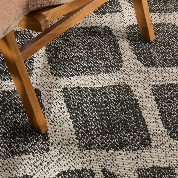 Close-up of a checkered patterned rug with wooden legs of a chair visible.
