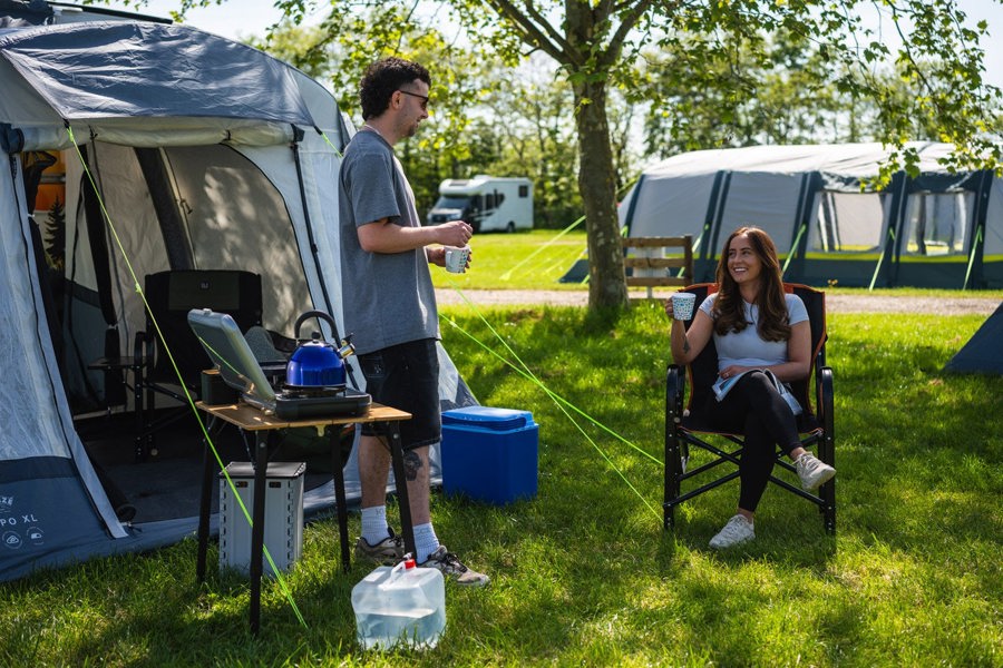 A couple enjoy the sun outside the Loopo Breeze® XL v2 Motorhome Awning, they are sitting in OLPRO camping furniture