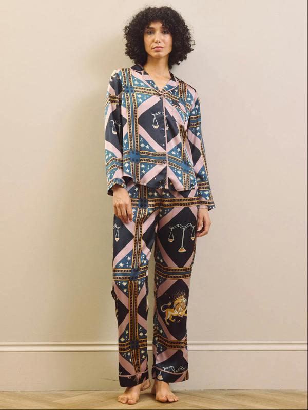 Woman wearing a celestial patterned satin pyjamas standing against a plain wall.