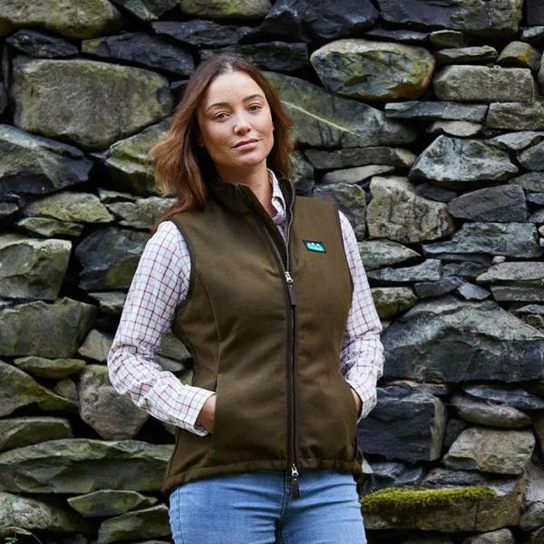 Woman wearing Ridgeline Womens Monarch gilet in moody teak standing by stone wall ideal for country pursuits