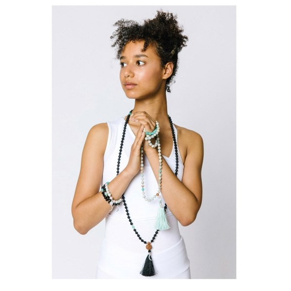 Woman wearing Kati Kaia Crystal Mala Necklace with black and turquoise beads and tassels holding beads in hands