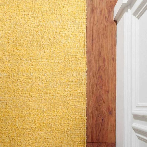 Transition from yellow carpet to wooden floor with white baseboard.