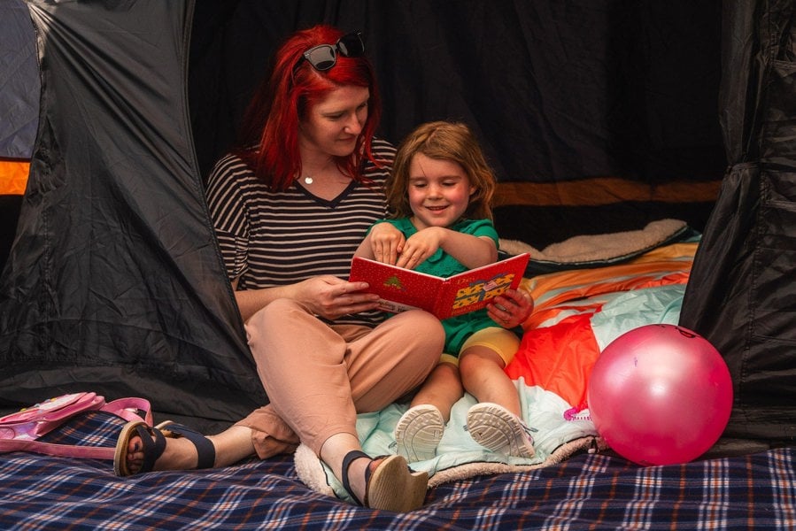 a mother & daughter read inside the Discovery Inflatable Tents sleeping pod, while sat on a blanko