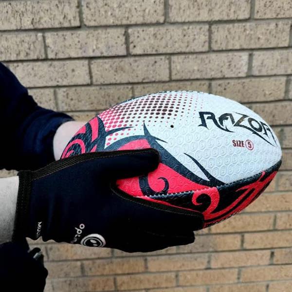 Hands in black Optimum Multi-X gloves holding a white and red Razor rugby ball against a brick wall - Optimum