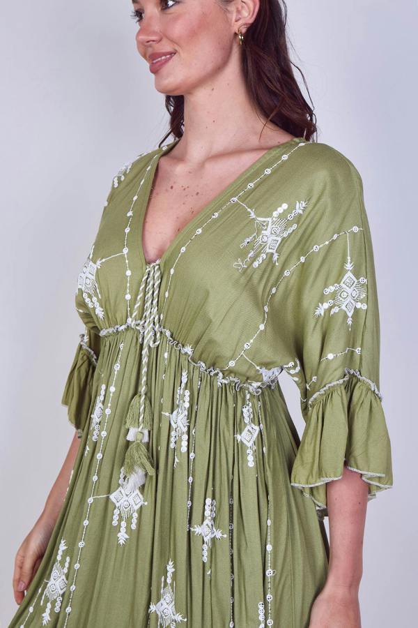 Woman wearing a green dress with white floral embroidery on a plain background