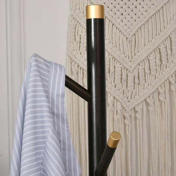 Coat rack stand with dark pole, gold top band, and angled hooks holding a light jacket