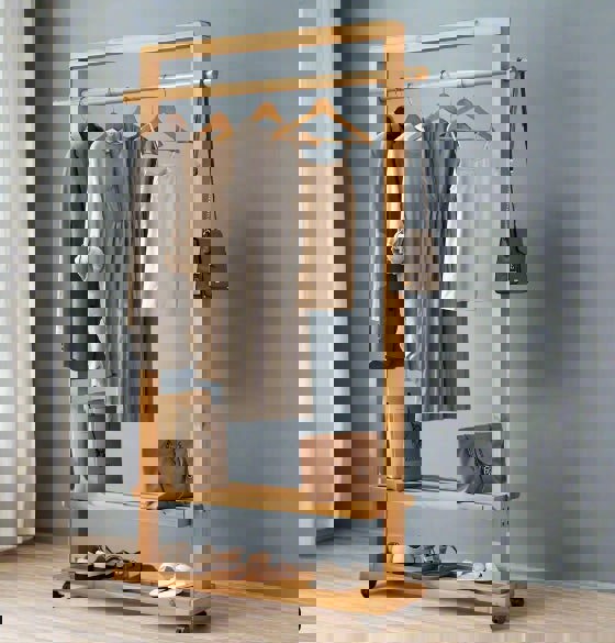 Wooden clothing rack with clothes and bags against a gray wall.