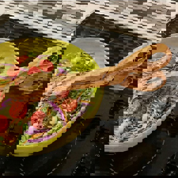 Closed olive wood serving tongs in a bowl of salad