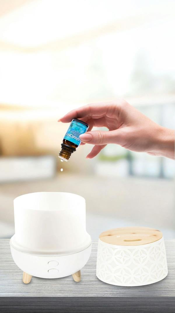 ladies hand dispensing harmony oil droplets into aroma diffuser placed on worktop with kitchen backdrop