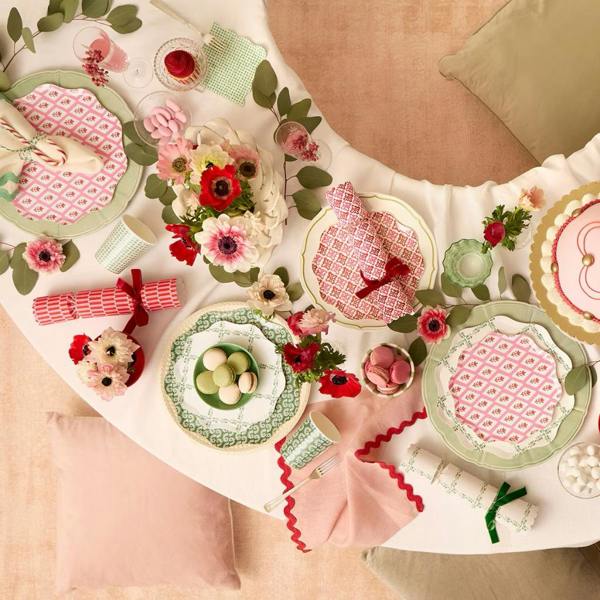 Overhead view of a festive Christmas table setting with block-print crackers, patterned paper plates, fresh flowers, and macarons.