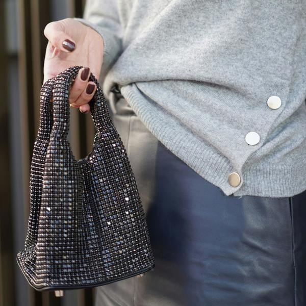 Close-up of a person holding a silver crystal-covered handbag with double grab handles.