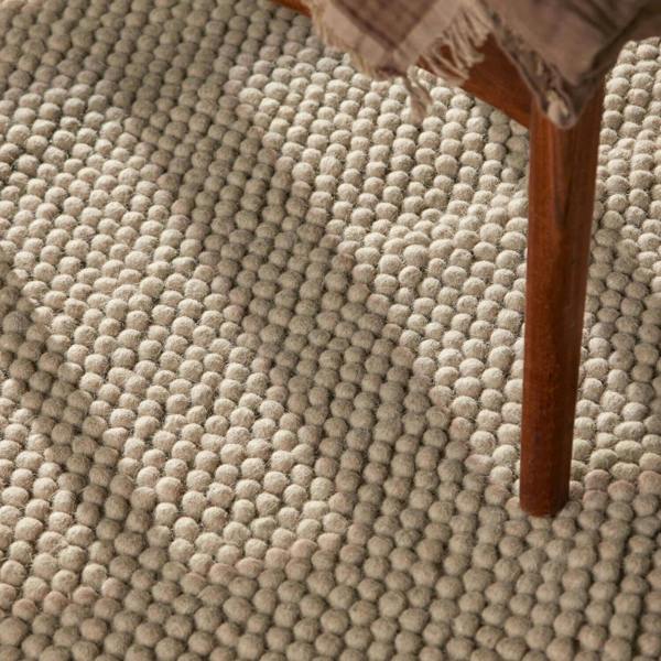 Close-up of a textured beige carpet with a wooden chair leg visible.