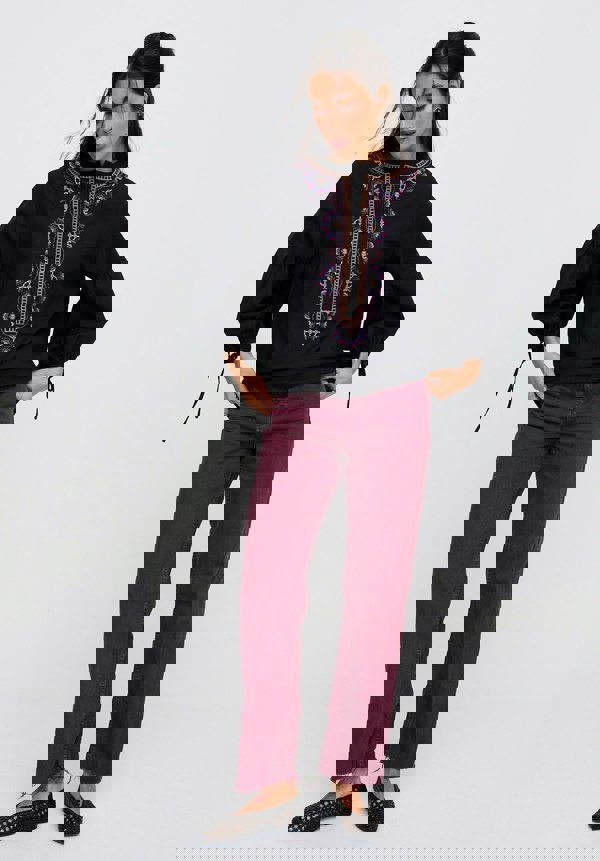 Woman wearing a black blouse with purple embroidery and burgundy pants on a white background