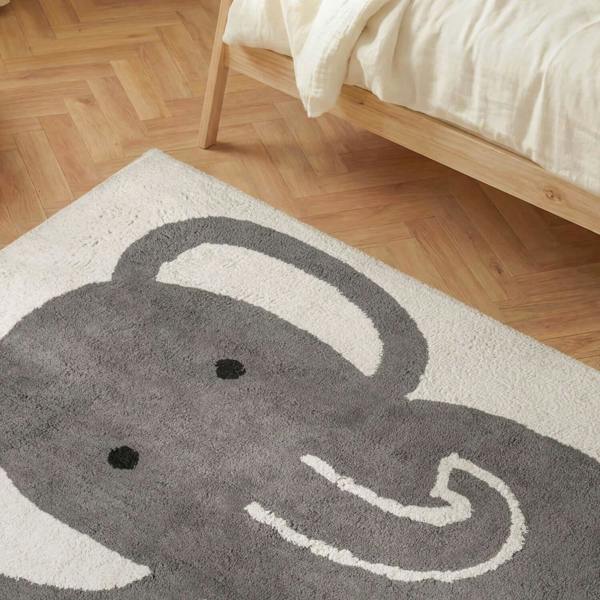 Gray elephant rug on a wooden floor next to a bed