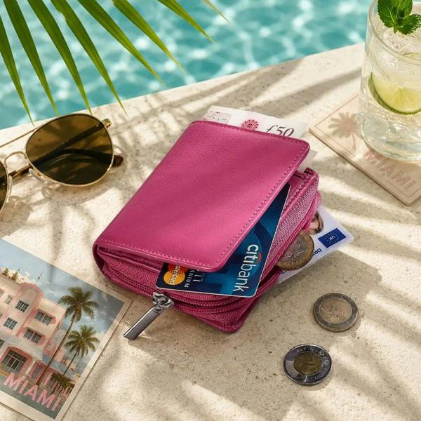 Pink wallet with cards and coins on a sandy surface near a pool