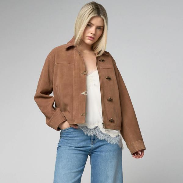 Image shows a woman wearing a real suede jacket which is tan in colour, with fireman claps to fasten. Jacket is modelled by a woman.