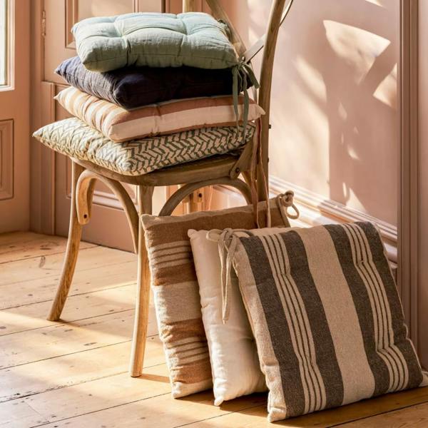 A stack of various neutral and striped linen seat pads on a wooden chair.