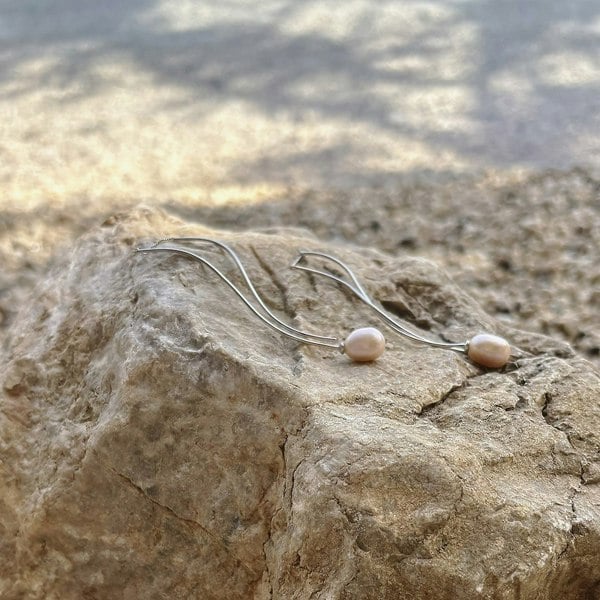 Wavy delicate earrings with pearls displayed in a beach setting.
