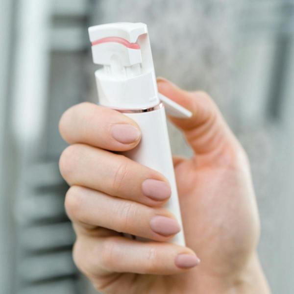 A hand with manicured nails and curled lashes holds the Rio WOW Lash Heated Eyelash Curler, poised for use against a blurred grey background.