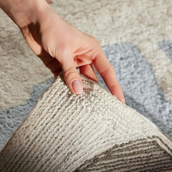 Hand holding a textured fabric sample against a patterned rug
