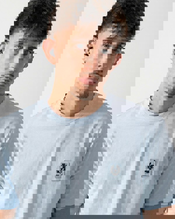 Man wearing a light blue t-shirt with a logo on a plain background