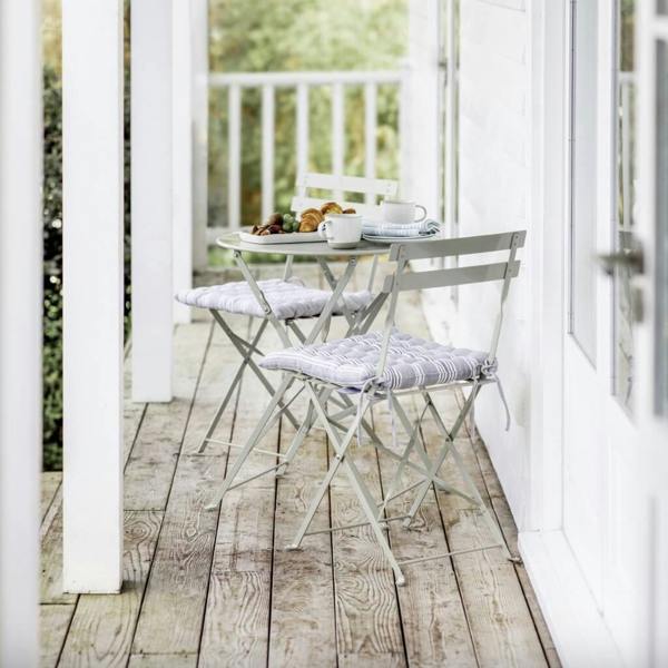 Clay grey metal folding bistro table and chairs styled on a weathered wooden veranda with breakfast pastries.