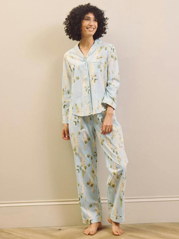Woman wearing a light blue floral pyjama set against a beige wall.